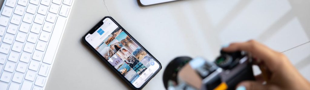 Person using vintage camera with smartphone and laptop in creative setup.